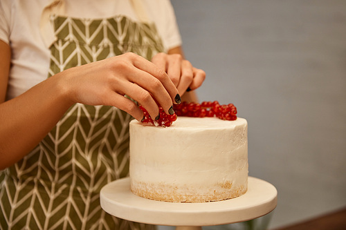 Cropped view of confectioner adding redcurrant on tasty cake with cream