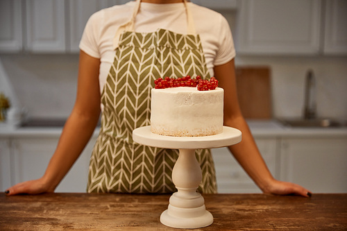 Cropped view of confectioner standing beside tasty cake with redcurrant on table
