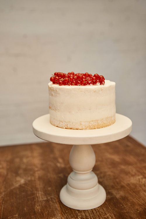Sweet sponge cake with cream and juicy redcurrant on cake stand on wooden table