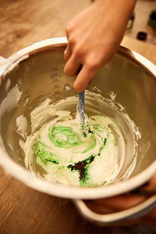 Cropped view of confectioner mixing cream with green food coloring in bowl