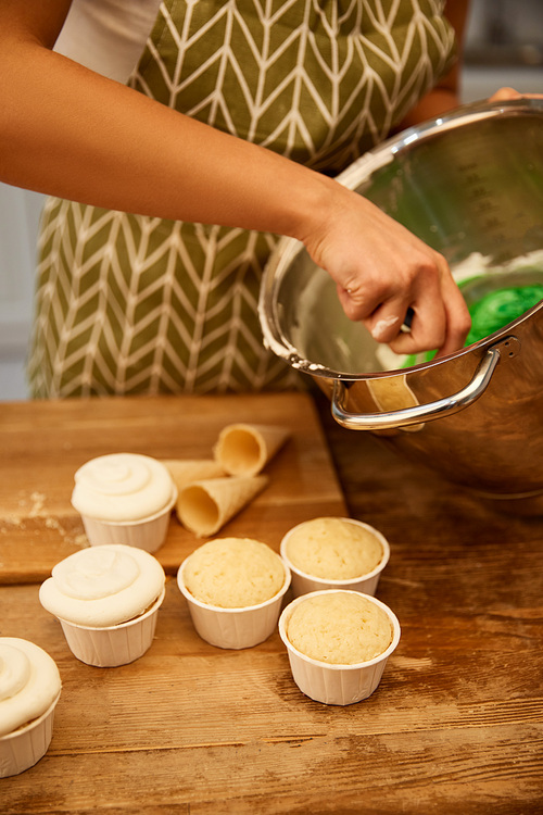 Cropped view of confectioner mixing cream for cupcakes and waffle cones on table