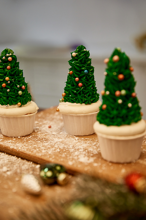 Selective focus of Christmas tree cupcakes with green cream and christmas balls with spruce branch on table