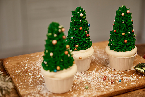 Selective focus of Christmas tree cupcakes with flour and christmas ball on cutting board