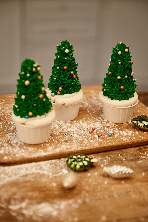 Tasty Christmas tree cupcakes with green cream and decorations on cutting board with christmas balls