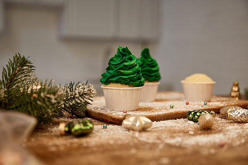 Tasty cupcakes with green cream on table with christmas balls and pine branch on table