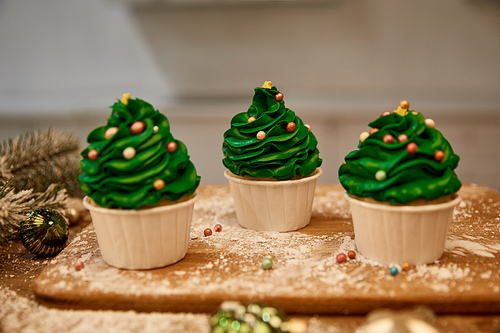 Decorated cupcakes with green cream and christmas balls with spruce branch on table