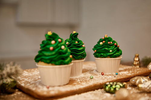 Selective focus of sweet cupcakes with christmas balls and spruce branch on cutting board