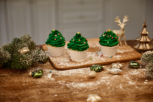 Cupcakes with sugar sprinkles and christmas balls with spruce branches on table