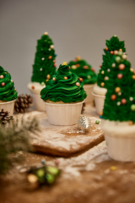 Selective focus of decorated Christmas tree cupcakes with sweet cream and spruce cones on table
