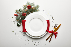 top view of festive Christmas table setting on white background with decorated pine branch and confetti
