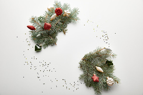 top view of festive Christmas decorated pine branches with baubles and confetti on white background