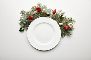 top view of white plate near festive Christmas tree branch with baubles on white background