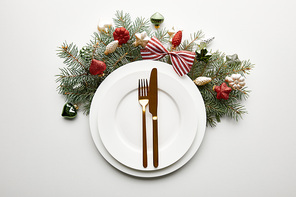 top view of white plates with cutlery near festive Christmas tree branch with baubles on white background