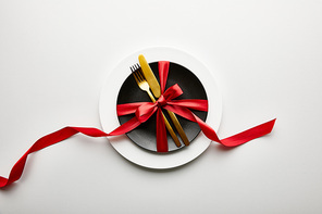 top view of white and black plates with cutlery and ribbon on white background