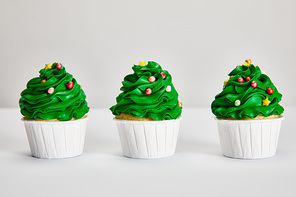 tasty Christmas tree cupcakes in row on white surface isolated on grey