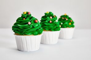 selective focus of tasty Christmas tree cupcakes in row on white surface isolated on grey