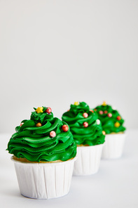 selective focus of tasty Christmas tree cupcakes in row on white surface isolated on grey