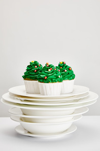 tasty Christmas tree cupcakes on white plates isolated on grey