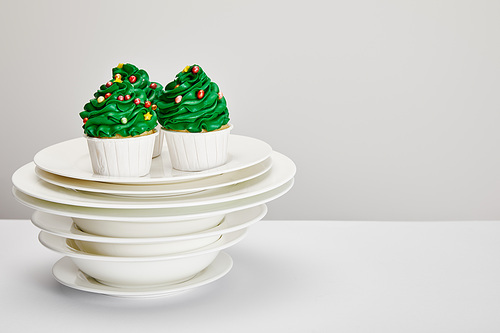 delicious Christmas tree cupcakes with plates on white surface isolated on grey