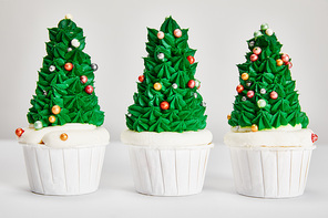 delicious Christmas tree cupcakes in row on white surface isolated on grey