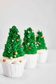 selective focus of delicious Christmas tree cupcakes in row on white surface isolated on grey