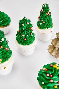 delicious cupcakes and decorative golden Christmas tree on white surface
