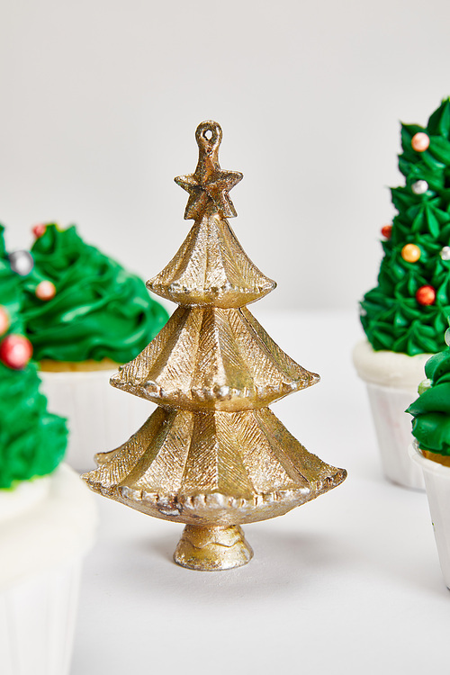 selective focus of delicious cupcakes and decorative golden Christmas tree on white surface isolated on grey