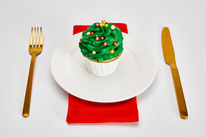 delicious cupcake on white plate with golden cutlery and red napkin on white surface