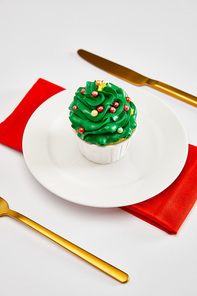 delicious cupcake on white plate with golden cutlery and red napkin on white surface