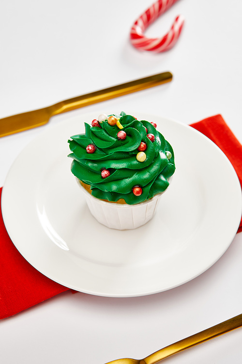 delicious cupcake on white plate with golden cutlery and red napkin on white surface