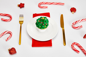 delicious cupcake on white plate with golden cutlery, candies, baubles and red napkin on white surface