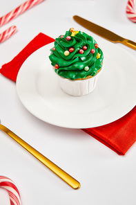 delicious cupcake on white plate with golden cutlery, candies and red napkin on white surface