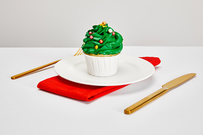 delicious cupcake on white plate with golden cutlery and red napkin on white surface isolated on grey