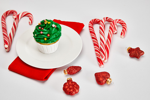 delicious cupcake on white plate with candies, baubles and red napkin on white surface