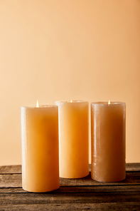 three festive burning candles on wooden table on beige