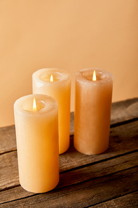 three burning candles on wooden table on beige