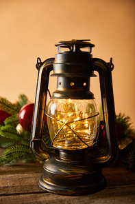 decorative retro oil lamp with lights, spruce branches and christmas balls on wooden table on beige