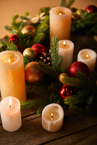 burning candles with spruce wreath and christmas balls on wooden table