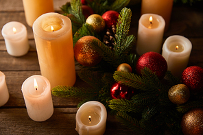 burning candles with spruce wreath, red and golden christmas balls on wooden table