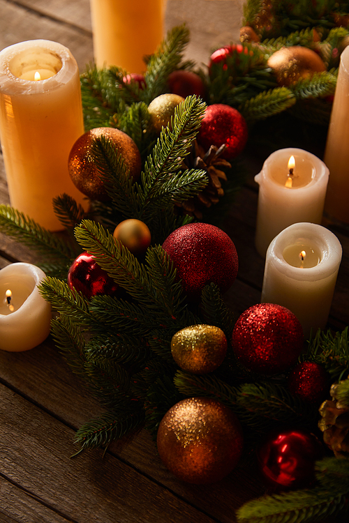 burning candles with spruce wreath and christmas balls on wooden table
