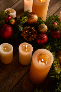 close up of burning candles with spruce branches and christmas balls on wooden table