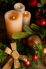 close up of burning candles with spruce branches, bow and christmas balls on wooden table