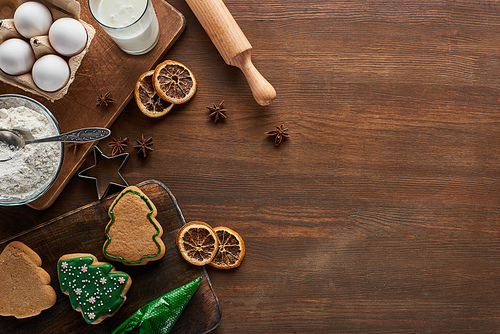 top view of delicious Christmas cookies near ingredients and spices on wooden table