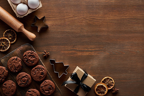 top view of chocolate Christmas cookies near gift box on wooden table