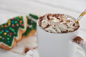 selective focus of Christmas cacao with cacao powder and whipped cream in mug with straw near cookies