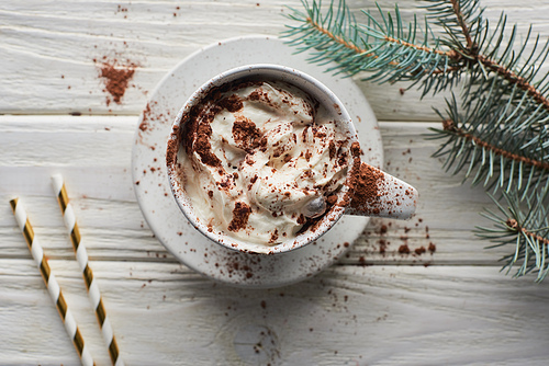 top view of Christmas cacao with cacao powder and whipped cream in mug on white wooden table near fir branch