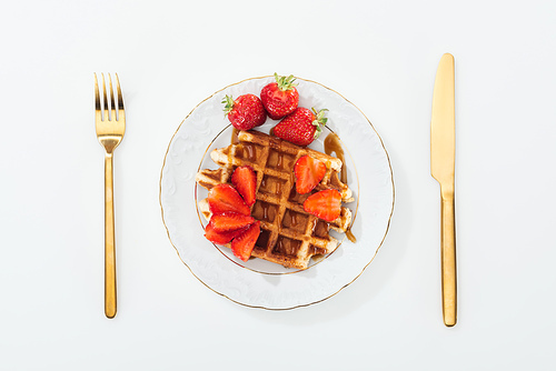 top view of waffle and strawberries on plate and fork with knife near plate