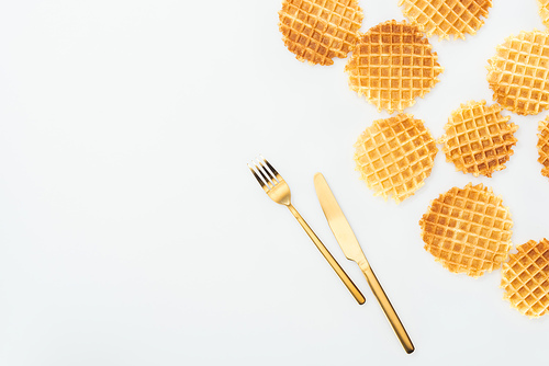 top view of scattered waffles and golden cutlery isolated on white