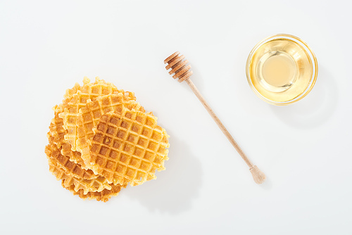 top view of waffles near wooden dipper and bowl with honey on white