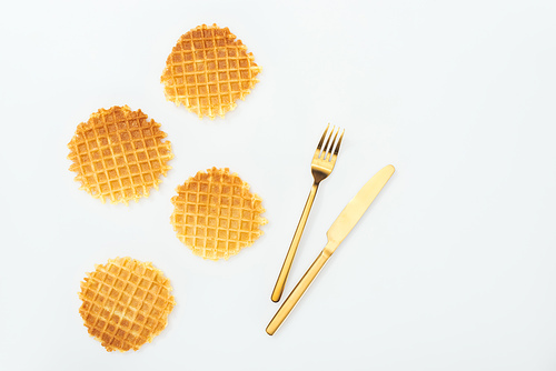 top view of four waffles near fork and knife isolated on white